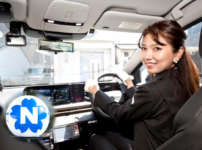 Smiling woman driving a modern car, hands on the steering wheel with a digital dashboard visible ahead.